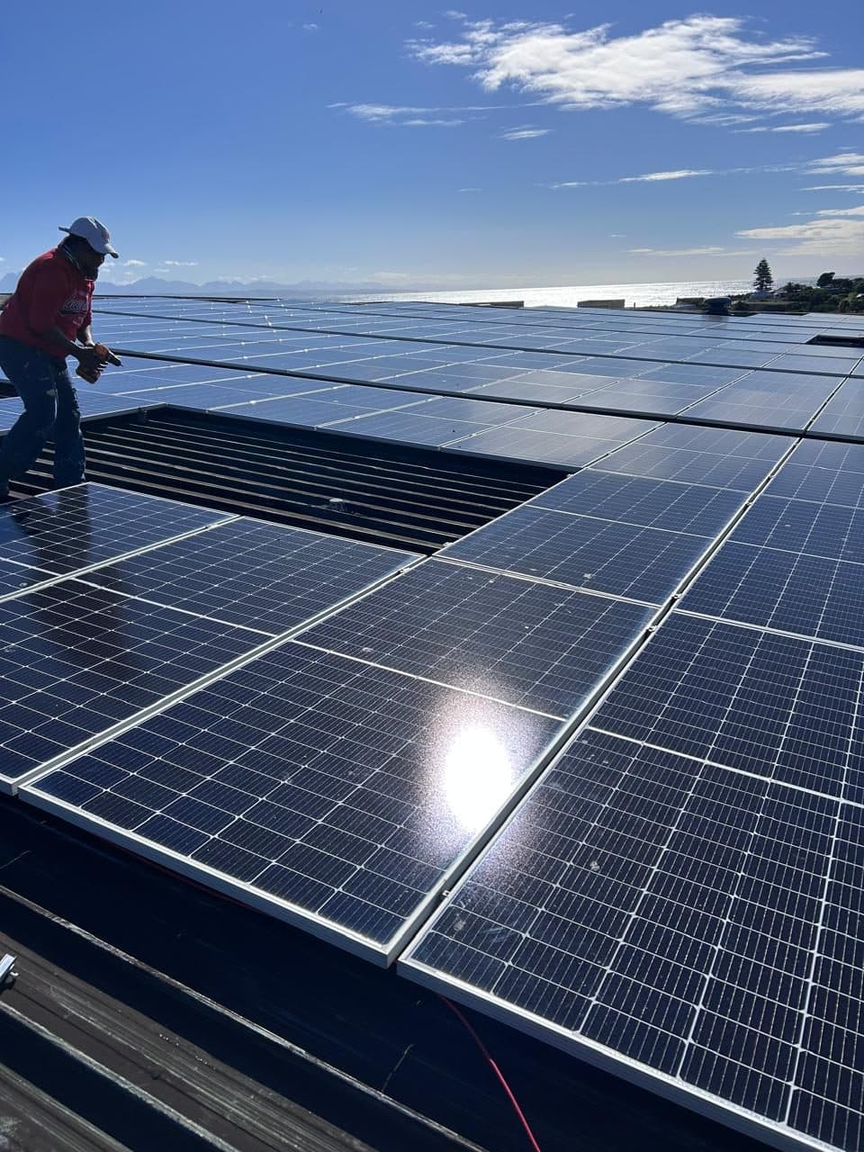 Sky Projects electrician installing a large commercial rooftop solar array overlooking the sea at Mossel Bay