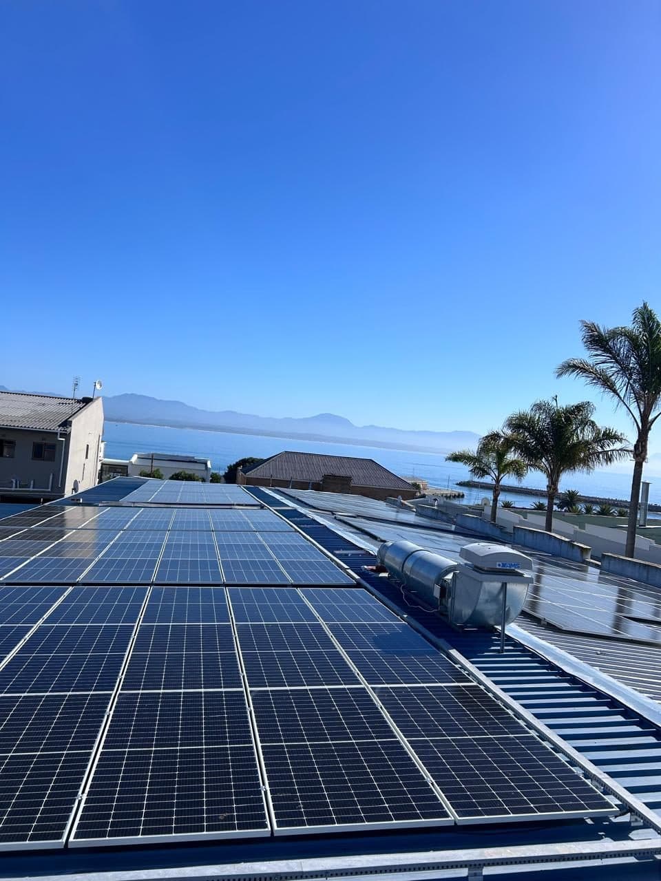 Rooftop solar panels overlooking the sea and palm trees in Mossel Bay, installed by Sky Projects